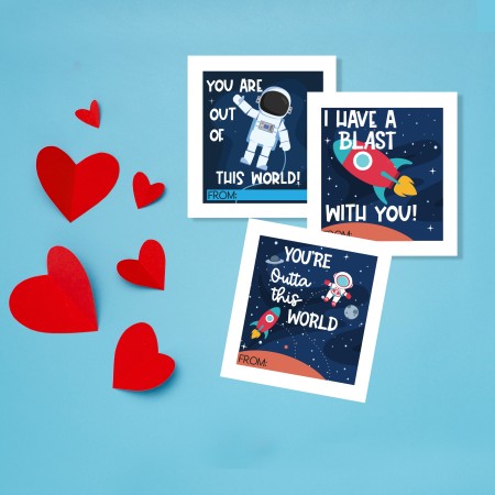 Printed space themed valentine cards on a blue paper background with hearts cut out from red paper