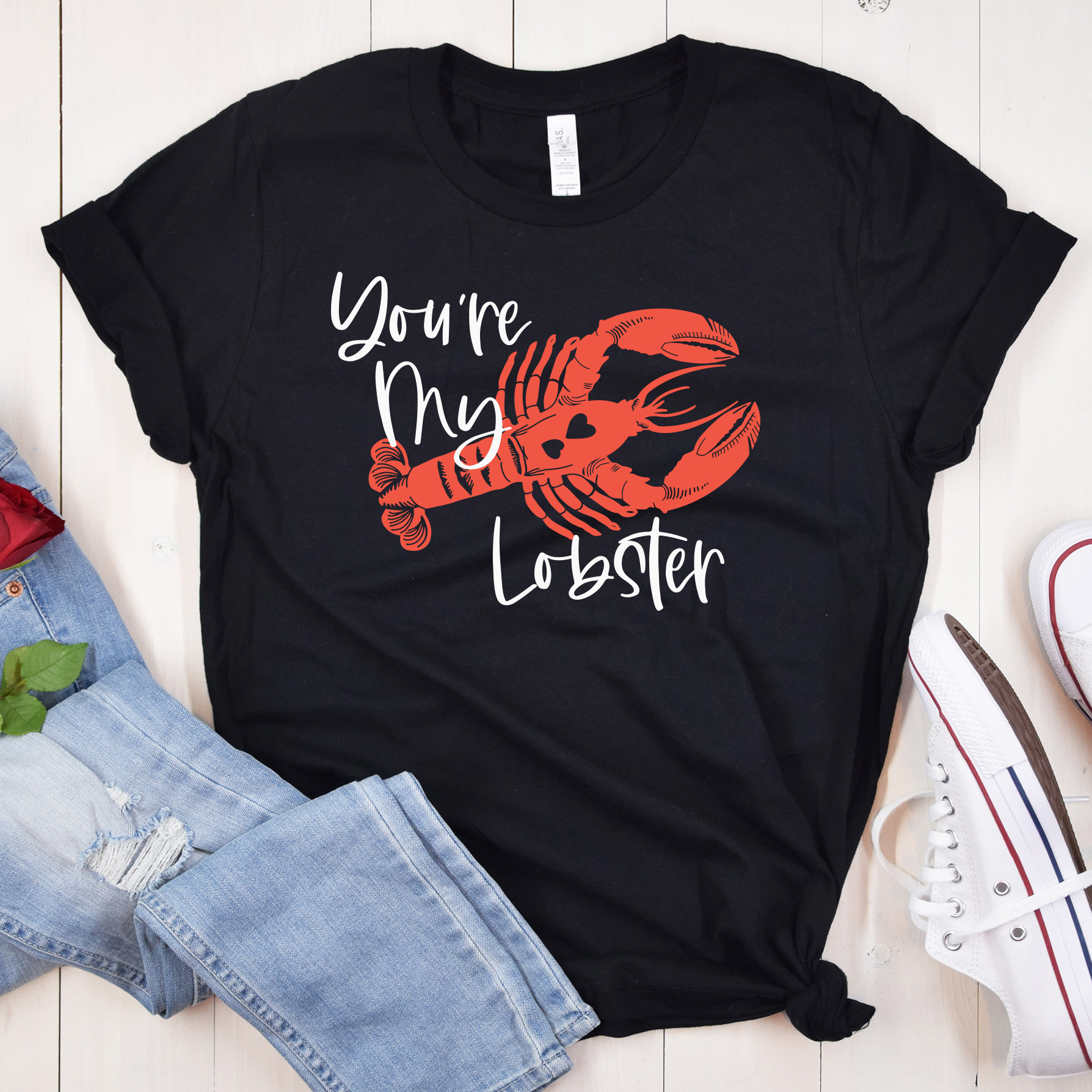 black shirt on a wood background with a design of a lobster. Above it is the text You're My Lobster.