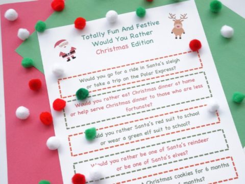 a paper of would you rather questions with a christmas theme. The paper is on top of red and green pieces of paper and Christmas colored pom poms.
