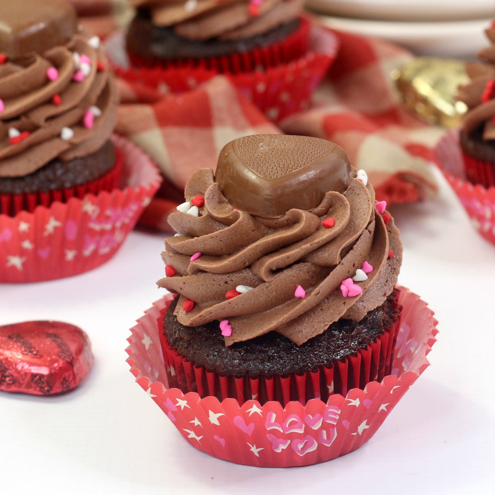 Valentines Day Chocolate cupcake with peanut butter chocolate frosting, heart shaped sprinkles, and a chocolate reeses treat on top.