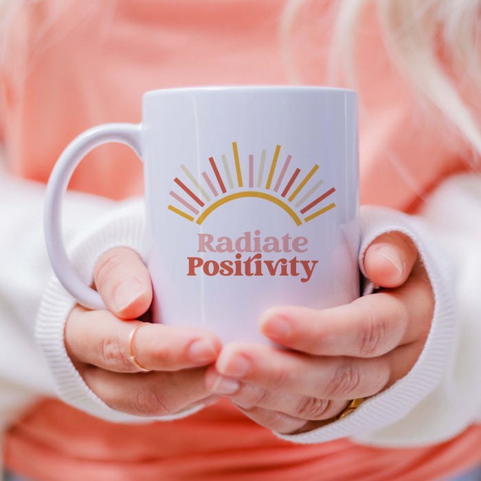 woman holding a white mug with the design of a sun shine and the text Radiate Positivity 