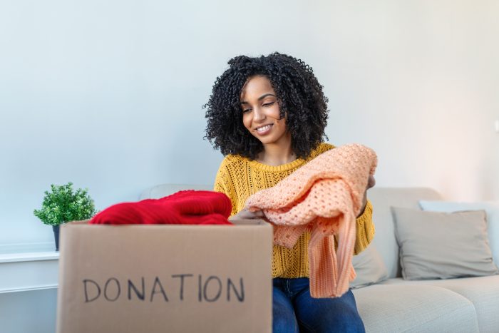 Woman holding cardboard donation box full with clothes. Concept of volunteering work, donation and clothes recycling.