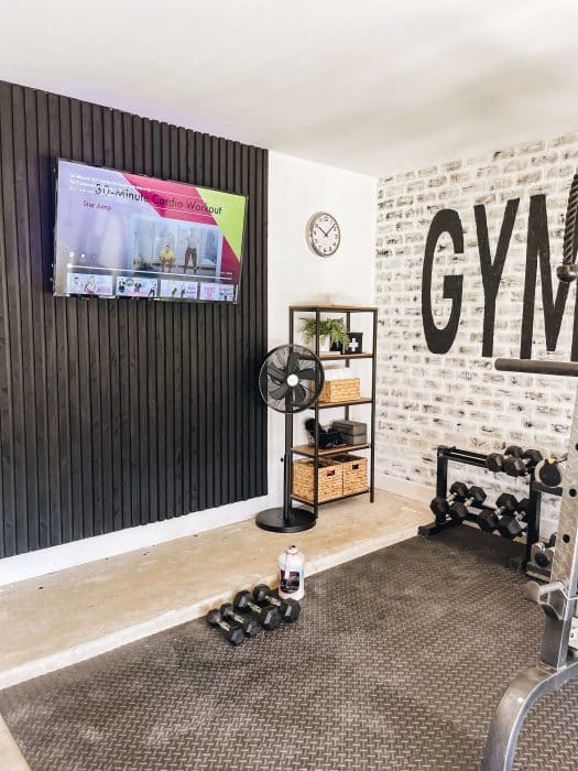 a beautiful home gym with a brick wall, vertical slat wall, and wall mounted tv