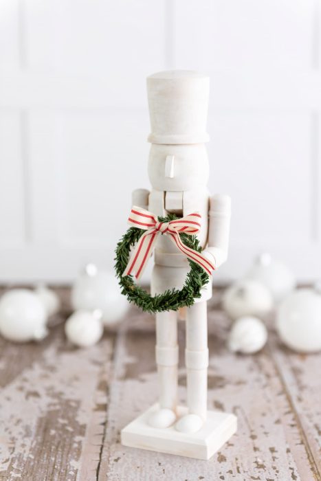 Modern nutcracker painted all white and holding a green wreath with a ribbon bow.