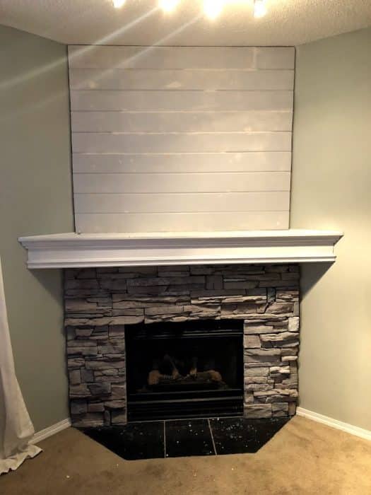 Stone corner fireplace with whitewashed stone. Process photo of adding shiplap to fill in the awkward space above the TV.