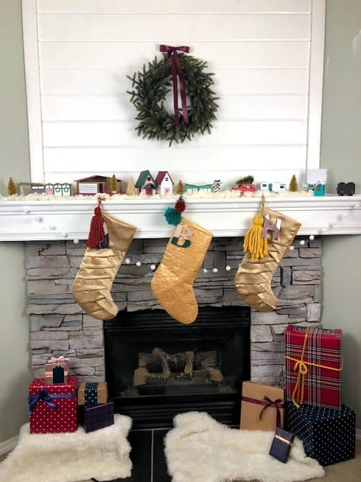 Stone corner fireplace with whitewashed stone and shiplap to fill in the awkward space above the TV. Decorated for Christmas with a wreath, stockings, and a midcentury modern paper house village.