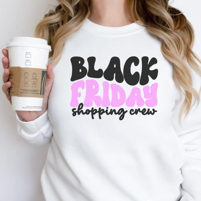 a woman in a white sweatshirt holding a starbucks coffee. Her crewneck sweatshirt has a black friday shopping crew written on it.