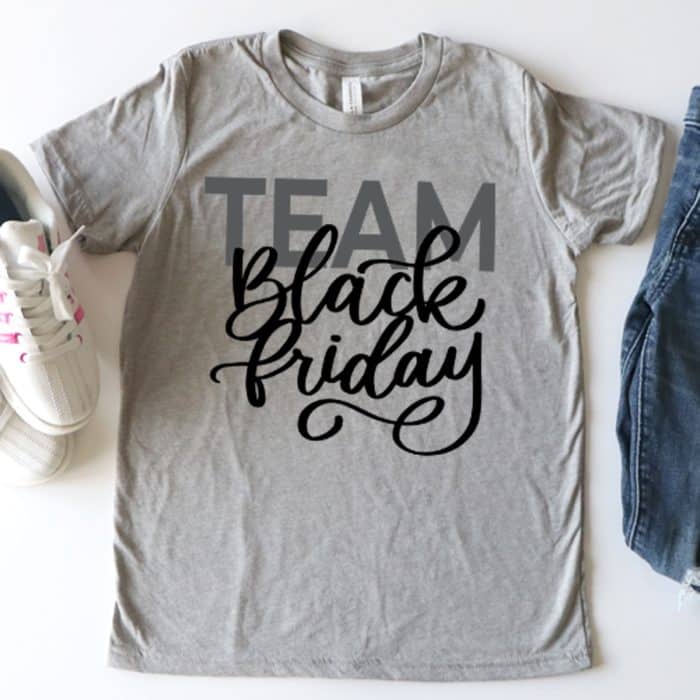 a grey tshirt on a white background with a pair of jeans and womens shoes. The shirt has a hand lettered calligraphy saying team black friday.