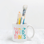white mug holding paint brushes with the text I can do hard things written on it in bright rainbow colors