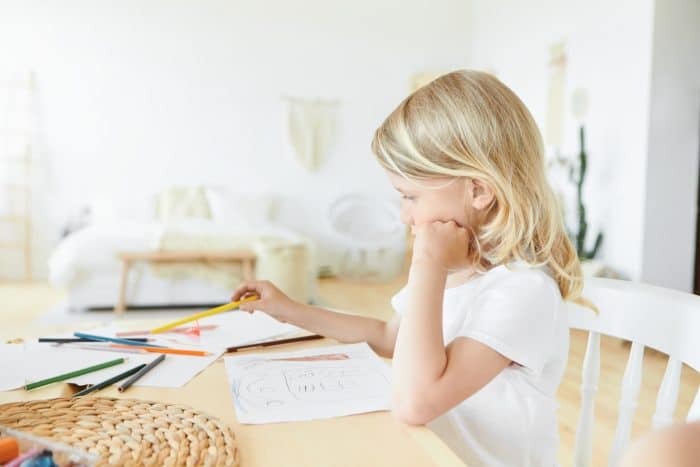 Young child sitting at a table with paper and colorful pencils.