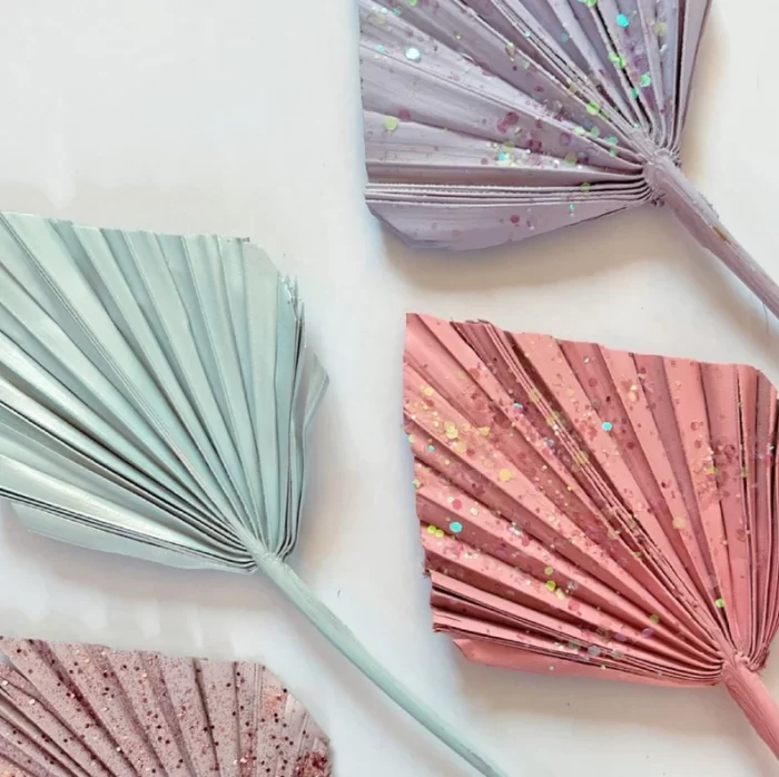 close up photo of paper palms painted pink, teal, and purple, and sprayed with glitter