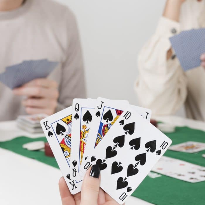 a group of people playing gard games with a close up of a hand holding 4 cards.