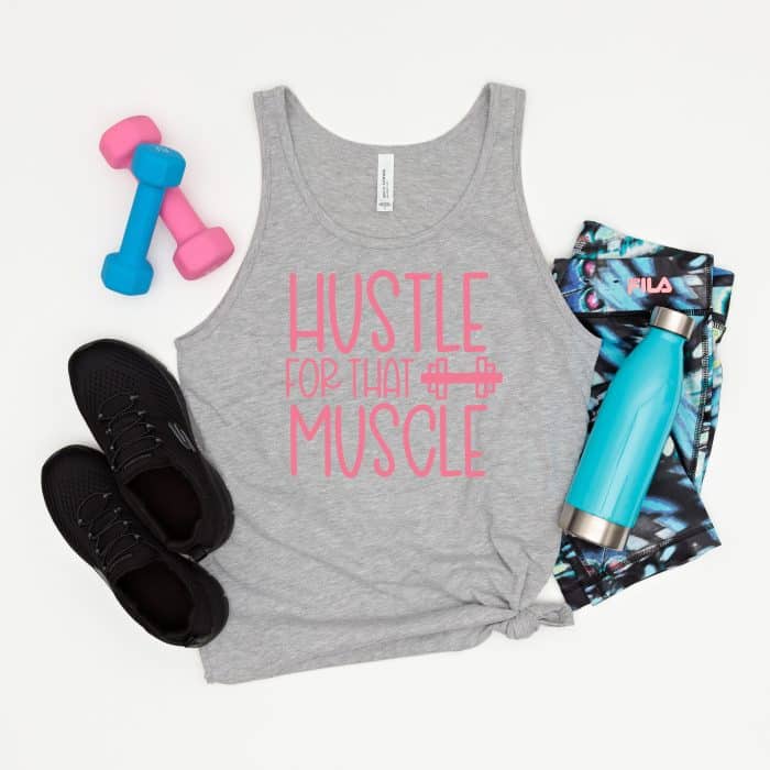 Athletic Grey tank top with Hustle For That Muscle written in pink text. Surrounded by pink and blue workout accessories.