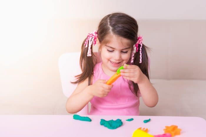 Portrait of Cute girl playing with toys for playdough near table.