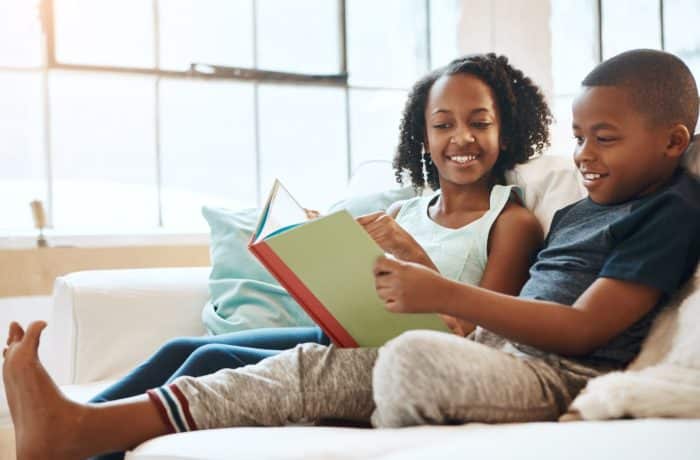 two kids sitting on a couch reading a book