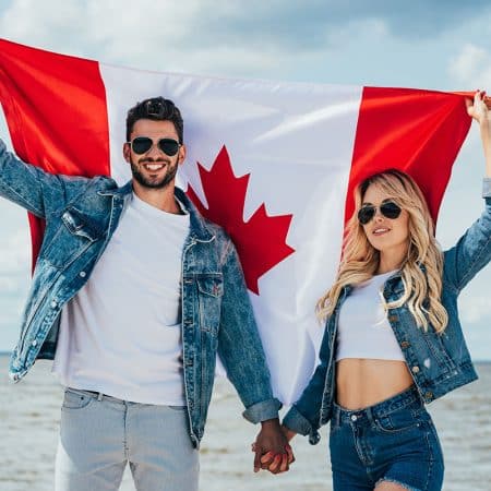 Couple holding a Canada Flag in front of a body of water.