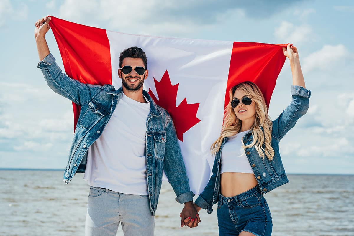 Couple holding a Canada Flag in front of a body of water.