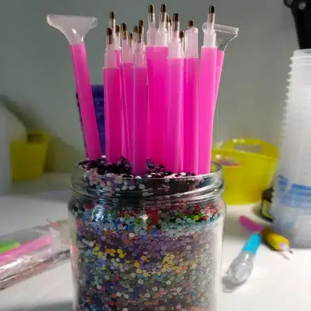 a jar filled with leftover diamonds from a diamond painting kit. It is being used to store diamond art pens.