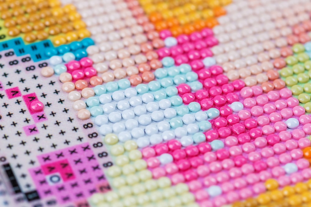 A close-up photograph of a diamond painting in progress, showcasing round drills arranged on a canvas. The drills are small, colorful, and sparkling, forming intricate patterns that resemble a beautiful mosaic.