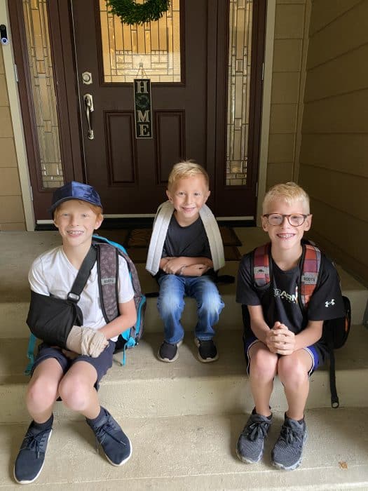 three boys sitting on a front step with backpacks on, leaving for their first day of school.