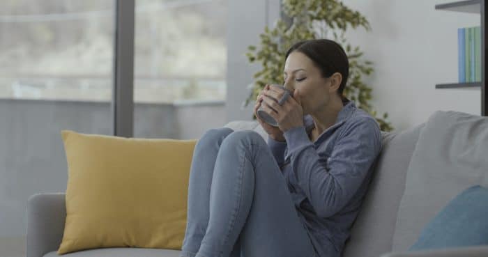 Young woman sitting on the couch at home and drinking a hot tea