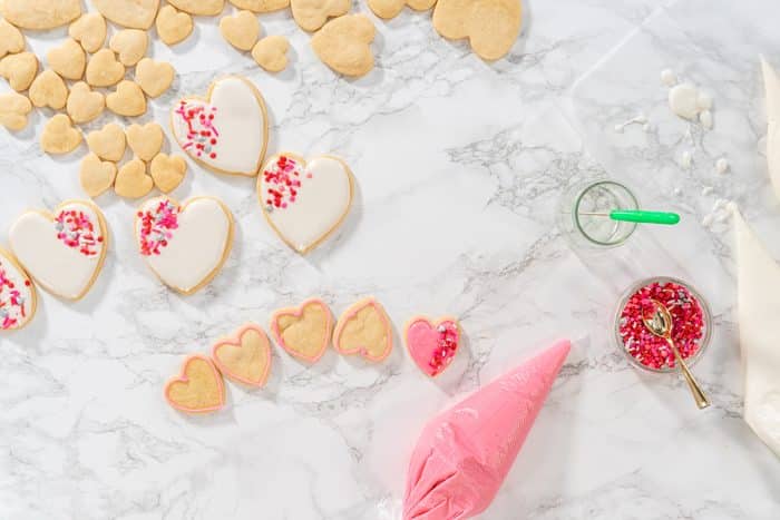 Flat lay. Decorating heart-shaped sugar cookies with pink and white royal icing for Valentine's Day.