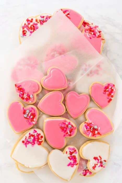 Storing valentines sugar cookies with pink and white royal icing in a large plastic container.